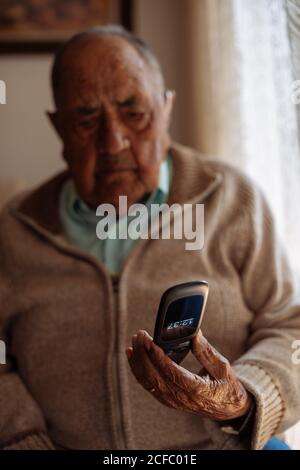 Älterer Mann, der sein Telefon in seinem Inneren benutzt Haus Stockfoto