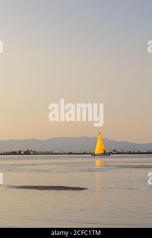 Helle Yacht geht unter gelbem Segel in ruhigem Wasser an sonnenaufgang auf Naturhintergrund Stockfoto