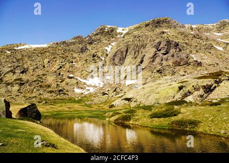 Ruhige schöne See zwischen grünen Rasen auf Hintergrund von steinigen Berg in sonnigen Tag Stockfoto