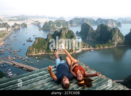 Von oben Blick auf liebevolles Paar, das sich hinlegt Metalldach und Beobachtung malerischer Blick auf Halong Bucht in Vietnam Stockfoto