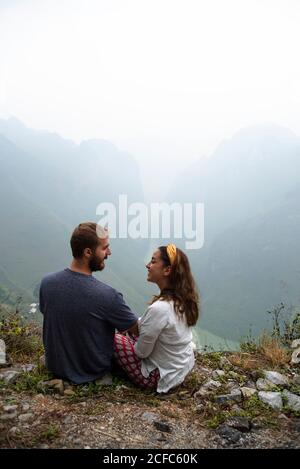Hohe Winkel Rückansicht der fröhlichen paar Touristen sitzen Auf felsigen Boden des Hügels und genießen Sie Urlaub im Hochland Lächelnd und einander anschauend Stockfoto