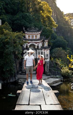 Ein paar Touristen in konischen Hüten, die auf einer Steinbrücke spazieren Führt zu einem schäbigen orientalischen Torbogen, während man den Urlaub genießt und schaut Aufeinander zu Stockfoto