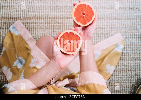 Draufsicht der Ernte anonyme Frau hält zwei frische lecker Halbe reife Grapefruit in den Händen, während sie auf dem Boden sitzen Auf dem Teppich Stockfoto