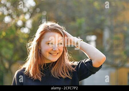 Junges Mädchen mit rötlichen Haaren und Sommersprossen steht im Freien und Lächelt auf das Kameraportrait Stockfoto