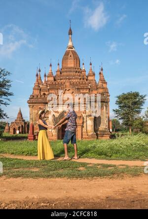 Seitenansicht des glücklichen jungen Paares in der Liebe, die Hände hält Beim Stehen neben dem schönen alten Tempel in Bagan Myanmar An sonnigen Tagen und genießen Sie Sommerferien Stockfoto