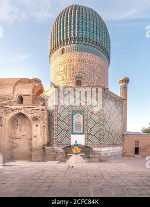 Rückansicht einer anonymen Frau, die am sonnigen Tag in Samarkand, Usbekistan, vor dem Mausoleum von Gur-e Amir mit schönen Ornamenten und einer Kuppel steht Stockfoto