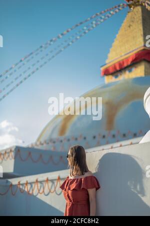 Seitenansicht einer Frau, die in der Nähe des buddhistischen Tempels mit dekorativen Girlanden und Turm unter bewölktem Himmel bei Tageslicht steht Stockfoto