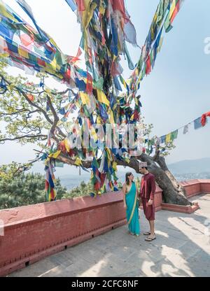 Seitenansicht des Paares in legerer Kleidung, das auf dem Damm läuft In der Nähe von alten buddhistischen Gebäuden unter farbenfroher Girlande mit Fahnen Sonniger Tag Stockfoto