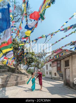 Seitenansicht eines Paares in legerer Kleidung, das in der Nähe von alt ist Buddhistische Gebäude unter farbenfroher Girlande mit Fahnen an sonnigen Tagen Stockfoto