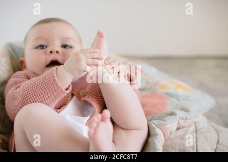 Charmant frech Baby in gestrickte Bluse auf Decke und liegen Kleine Füße beim Betrachen der Kamera im hellen Raum Stockfoto