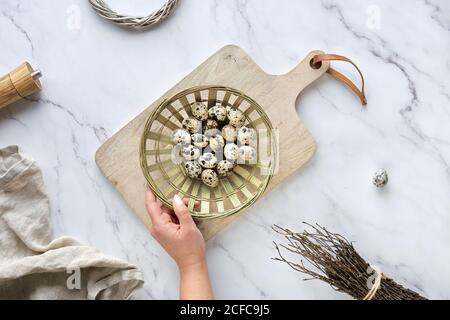 Null Abfall Ostern Hintergrund auf Marmortisch. Wachtel Ostereier und natürliche Frühlingsdekorationen und Eukalyptuszweige. Hand hält Rattang Platte mit Stockfoto