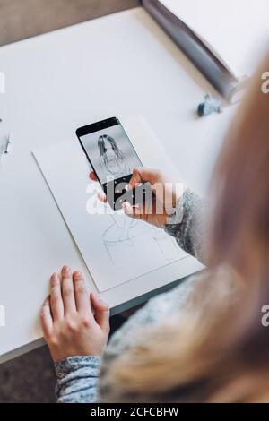 Von oben Ernte blonde Mädchen Foto auf Handy Der ersten Skizze auf Papier am Tisch im Büro Stockfoto