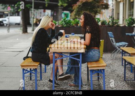 Seitenansicht von schönen jungen Frauen, die in der Berliner Straße sitzen Cafe reden und lachen Stockfoto