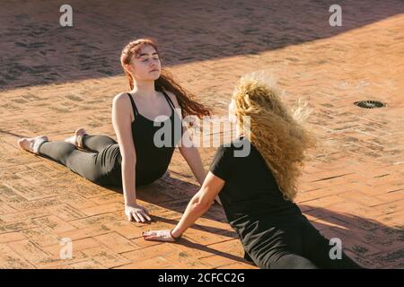 Hoher Winkel von jungen und mittleren Alters Frauen in schwarz Sportbekleidung, die Cobra posiert, während sie gemeinsam Yoga bei Sonnenschein praktiziert Terrasse Stockfoto