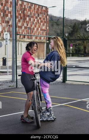Seitenansicht diverser Sportlerinnen, die neben dem Fahrrad stehen und lachen Bei Witz, während das Wochenende genießen und einander anguck Stockfoto