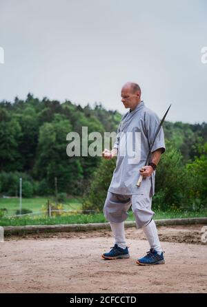 Bestimmt Mann mittleren Alters in Kimono Fokussierung und mit Schwert Beim Training allein im Garten Stockfoto