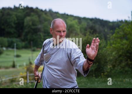 Bestimmt Mann mittleren Alters in Kimono Fokussierung und mit Schwert Beim Training allein im Garten Stockfoto