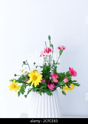 Frühlingsstrauß mit Gänseblümchen und Ranunculus, buntes Bouquet in weißer Vase, Instagram-Stil, Stockfoto