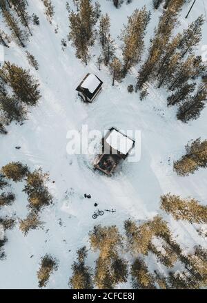 Luftaufnahme von oben auf kleine Holzfällerhütten, die sich inmitten von Schnee befinden Kiefernwald in der finnischen Landschaft Stockfoto