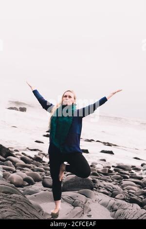 Junge Frau mit aufgespannten Händen meditiert und steht auf Felsen in der Nähe der Küste Stockfoto