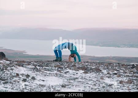 Seitenansicht einer blonden Frau mit hochgepupptem Bein und von Hand zu Seite posiert sie auf dem Berg im Schnee Stockfoto