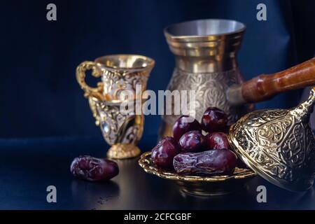 Bio getrocknete Datteln in traditionellen arabischen goldenen Teller, Tasse Kaffee oder Tee. Iftar Heiligen Monat Ramadan Konzept. Selektiver Fokus. Speicherplatz kopieren. Darck Bac Stockfoto