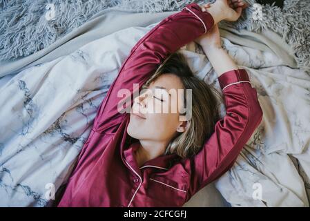 Junge hübsche Frau im Schlafanzug lächelt, während sie im Schlafzimmer auf dem Bett schläft Stockfoto