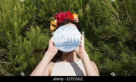 Junge Frau mit einem Spiegel im Gesicht vor grünem Hintergrund Stockfoto