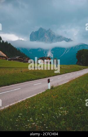 Autobahn neben Cottage Village auf einem Hügel in der Nähe von grünen dichten Wald Gegen schöne Nebelberge in den Dolomiten im Sommer bewölktes Wetter Stockfoto