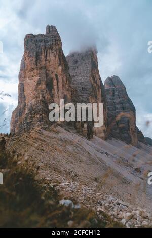 Unglaubliche Aussicht von den Ausläufern mit grünem Gras und kleinen Felsen Von nebligen Gipfeln der Berge drei Zinnen in den Dolomiten während Bewölktes Wetter Stockfoto