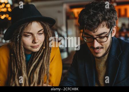 Ein intelligenter Mann in einer Brille und eine elegante Frau in einem Hut blicken auf den Monitor, während der Mann im Café auf dem Laptop tippt Stockfoto