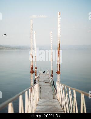 Schmaler Pier mit verwitterten Geländern und entfernter Reisender befindet sich in der Nähe Ruhiges Meerwasser gegen wolkenlosen Himmel Stockfoto
