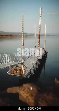 Alte rostige Pier mit entfernten Touristen in der Nähe des friedlichen Meeres Wasser in der Dämmerung Stockfoto