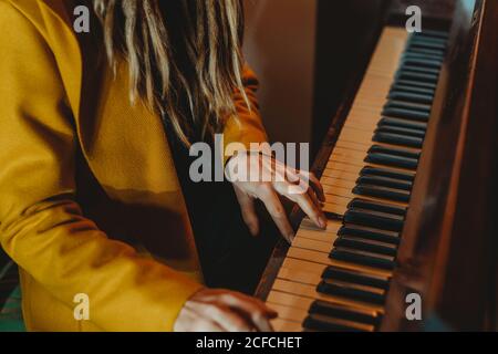 Cropped unkenntlich Hipster weiblich mit Dreadlocks tragen gelben Mantel spielen Klavier, während man in einem Zimmer im Retro-Stil sitzt Stockfoto