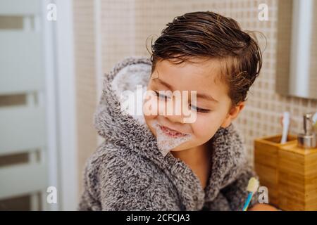 Entzückendes Kind trägt kuscheligen Bademantel im Badezimmer mit Zahnbürste stehen Stockfoto