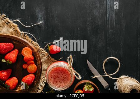 Blick von oben auf leckeren hausgemachten Erdbeersaft im Glas Platziert in der Nähe Schüssel mit reifen Beeren auf schwarzem Holzhintergrund Stockfoto
