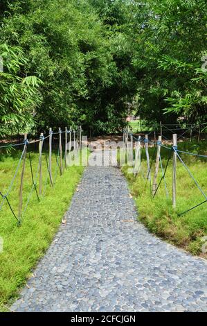 Perspektivischer Blick auf einen gepflasterten, sensorischen Fußweg aus glatten, abgerundeten Kieselsteinen mit einem rustikalen Seilzaun in einem ländlichen botanischen Garten. Stockfoto