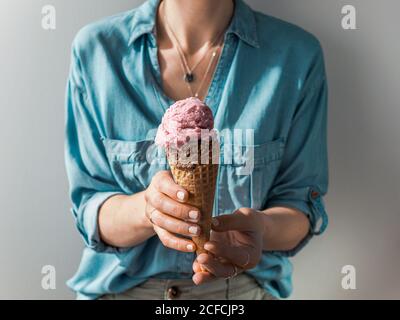 Eis in der Hand im Kegel halten. Eisportionierer in den Händen der Frau Stockfoto
