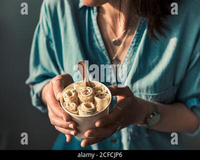 Gerolltes Eis in Kegelbecher in Frauenhänden. Frau in Jeans-Hemd hält Kegelbecher mit thai-Stil Vanille gewalzte Eis Stockfoto