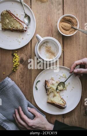 Draufsicht auf gesichtslose Dame, die Teller mit Kuchenscheibe hält Am Holztisch mit leckeren Stücken veganer Zitrone und Kokosnusskuchen beim Frühstück Stockfoto