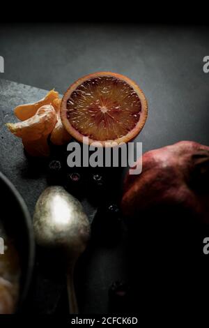 Von oben Chia Samen Pudding mit Scheiben von Orange, Mandarinen und Oliven in Schüssel neben Löffel und Grapefruit auf dunklem Tisch Stockfoto