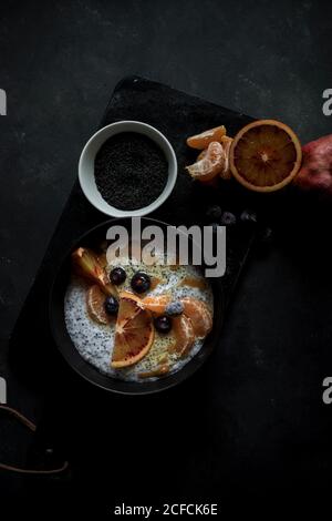 Von oben Chia Samen Pudding mit Scheiben von Orange, Mandarinen und Oliven in Schüssel neben Löffel und Grapefruit auf dunklem Tisch Stockfoto