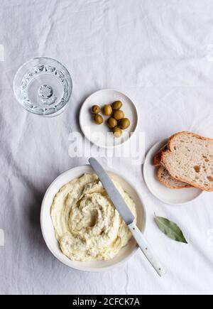 Von oben Schüssel mit Kabeljau Brandade in der Nähe von Oliven, Brotscheiben und Lorbeerblättern auf einem Küchentisch weißen Hintergrund platziert Stockfoto