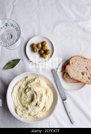 Von oben Schüssel mit Kabeljau Brandade in der Nähe von Oliven, Brotscheiben und Lorbeerblättern auf einem Küchentisch weißen Hintergrund platziert Stockfoto