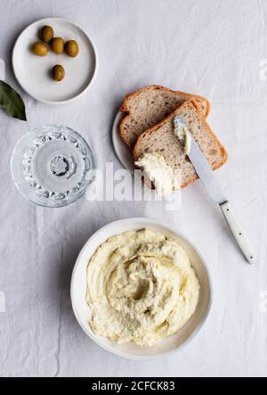 Von oben Schüssel mit Kabeljau Brandade in der Nähe von Oliven, Brotscheiben und Lorbeerblättern auf einem Küchentisch weißen Hintergrund platziert Stockfoto