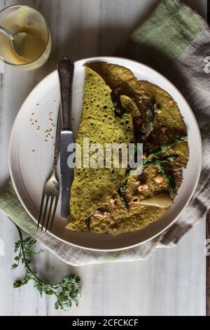Draufsicht auf weißen Teller mit Haferkrepe mit Spargel Und Tahini-Paste serviert auf rustikalem Brett mit Grüns Stockfoto