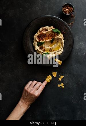 Draufsicht auf unkenntlich Person Hand hält stilvolle schwarze Platte Mit köstlichen frischen Auberginen und Blumenkohl Dip stilvoll dekoriert mit Bunte Gewürze und Minzblätter Stockfoto