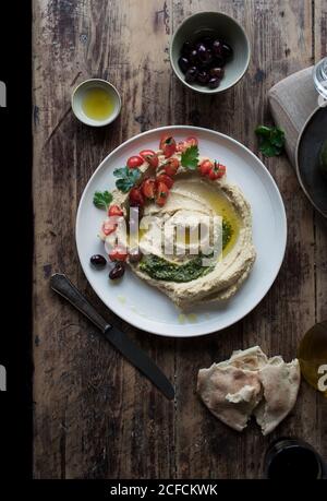 Von oben Platte von köstlichen Pesto Hummus mit Kirsche verziert Tomaten und Bohnen mit Petersilie auf Holzplatte in der Nähe platziert Fladenbrot und Öl Stockfoto