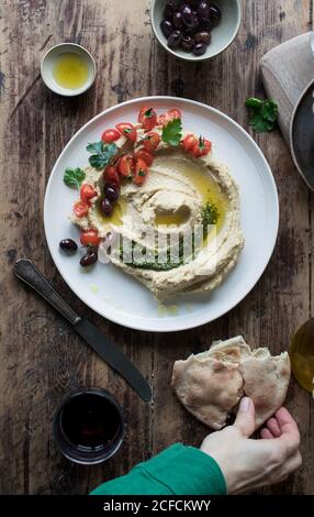 Von oben Platte von köstlichen Pesto Hummus mit Kirsche verziert Tomaten und Bohnen mit Petersilie auf Holzplatte in der Nähe platziert Fladenbrot und Öl Stockfoto