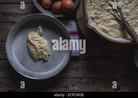 Von oben Auflaufform mit Teig zum Kochen Kuchen auf Schneidebrett und Eier auf Holzhintergrund Stockfoto